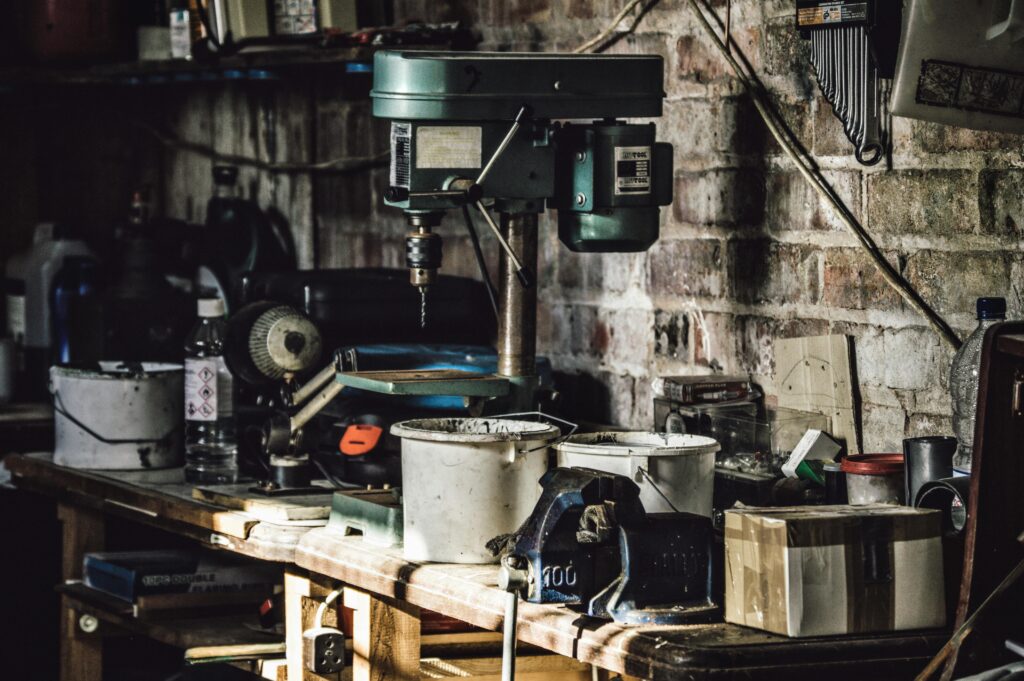 pexels-photo-115558-115558 A detailed view of a cluttered workshop with a focus on a drill press and various tools.
