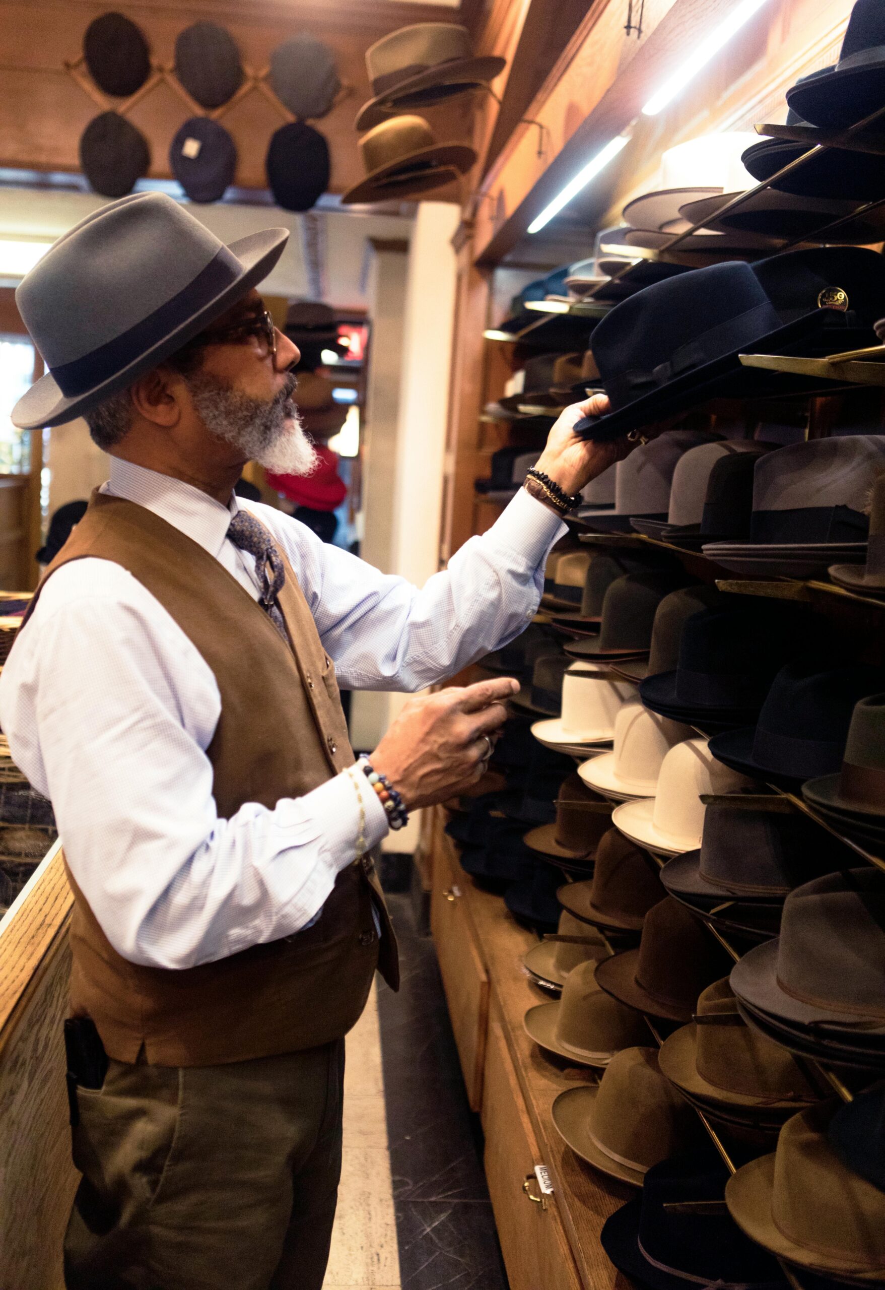 pexels-photo-936038-936038 An adult man selects a hat from a variety displayed on shelves inside a stylish store.